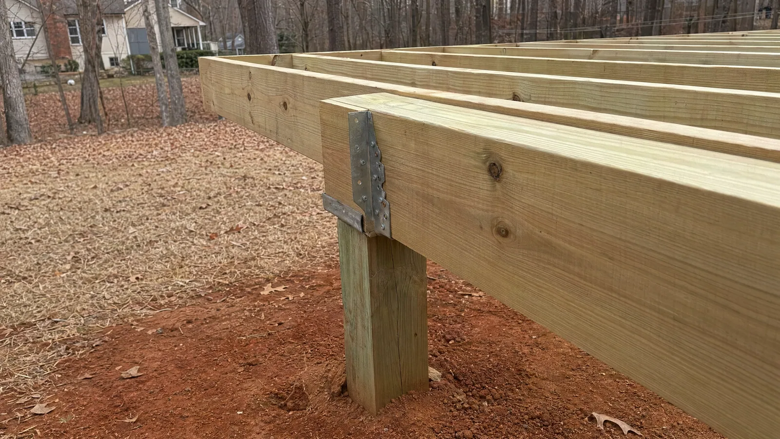 Partial view of deck framing in a Raleigh backyard during cool fall weather, showing pressure-treated joists and dry native clay soil