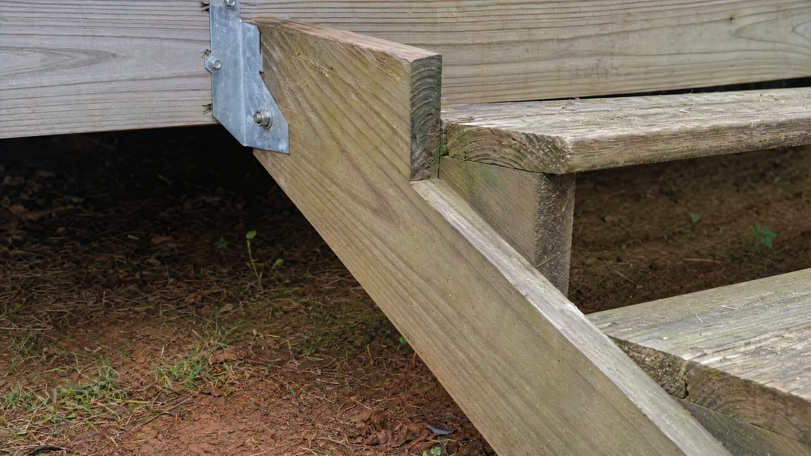 Close-up inspection detail of a deck stair stringer attached to a deck frame with metal hardware, showing treads and connection points during a deck stair rebuild in Raleigh NC
