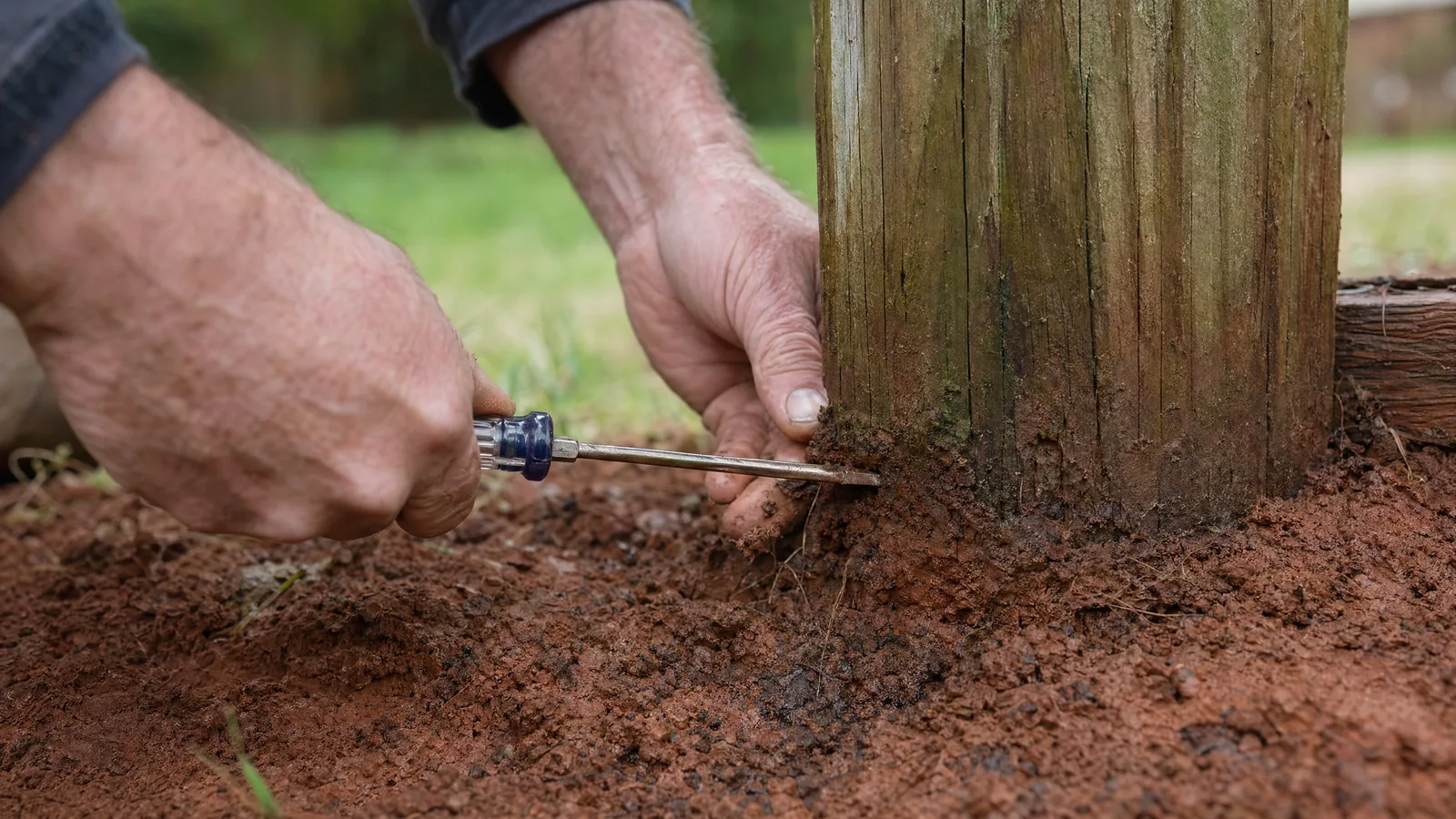 Contractor inspecting a deck post base in red clay soil for rot and moisture damage during a deck assessment in the Raleigh area.