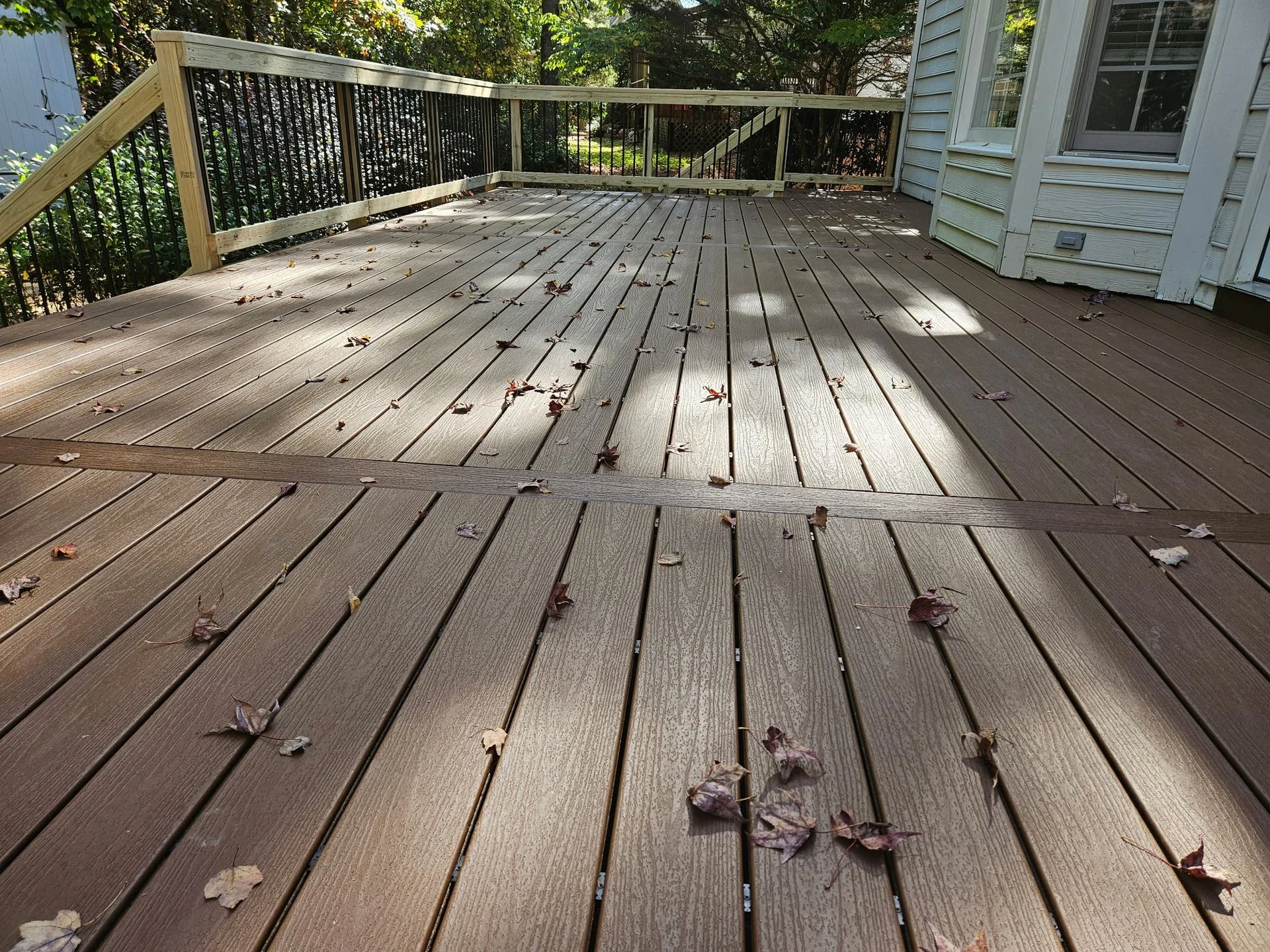 Composite deck with decorative inlay strip and black aluminum balusters, fall leaves on the surface
