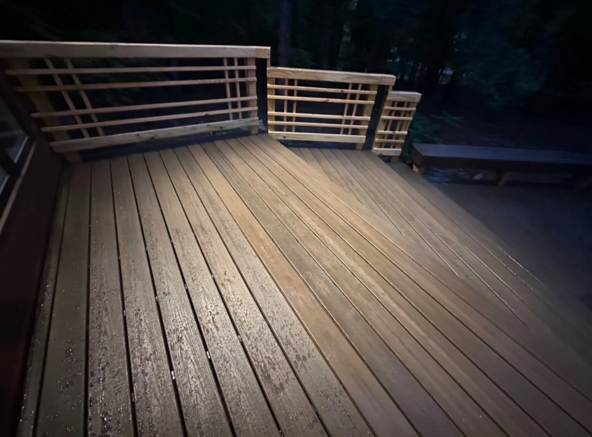 Two-level composite deck with horizontal black railing, wet surface at dusk