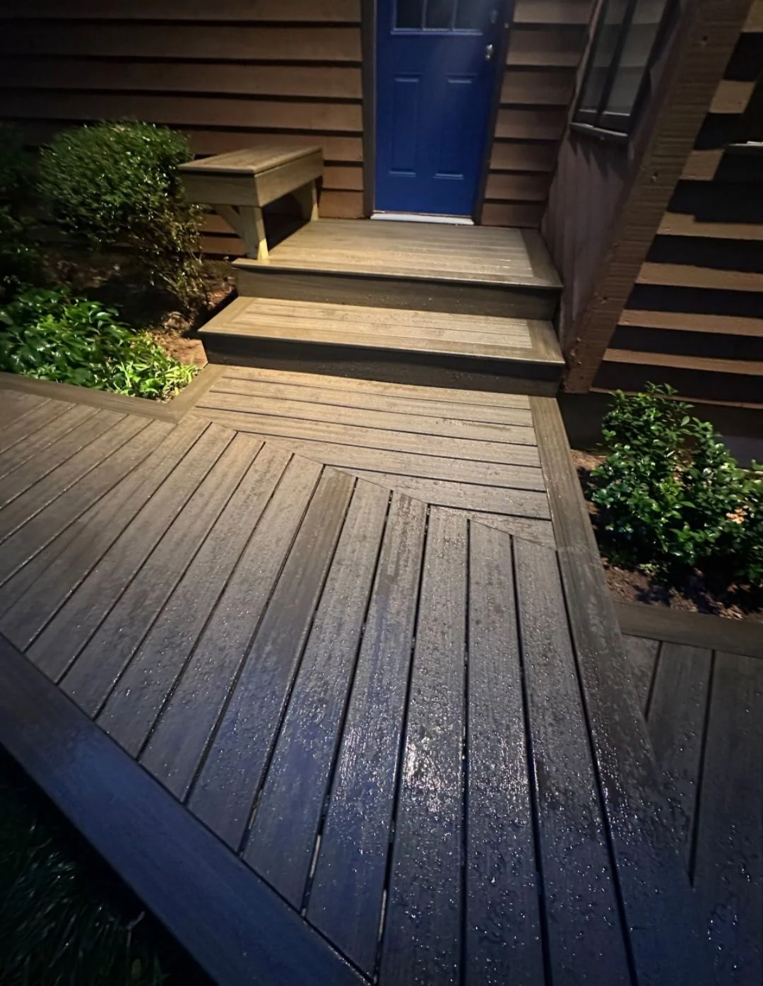 Front entry composite deck with herringbone inlay pattern and dark steps to a blue front door at night